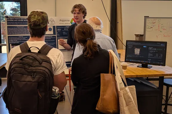 Thomas McCoy talks with three visitors in front of his poster, which carries the Mines and Argonne National Laboratory logos. On the table beside him, a monitor shows his 3-D neutron viewer.